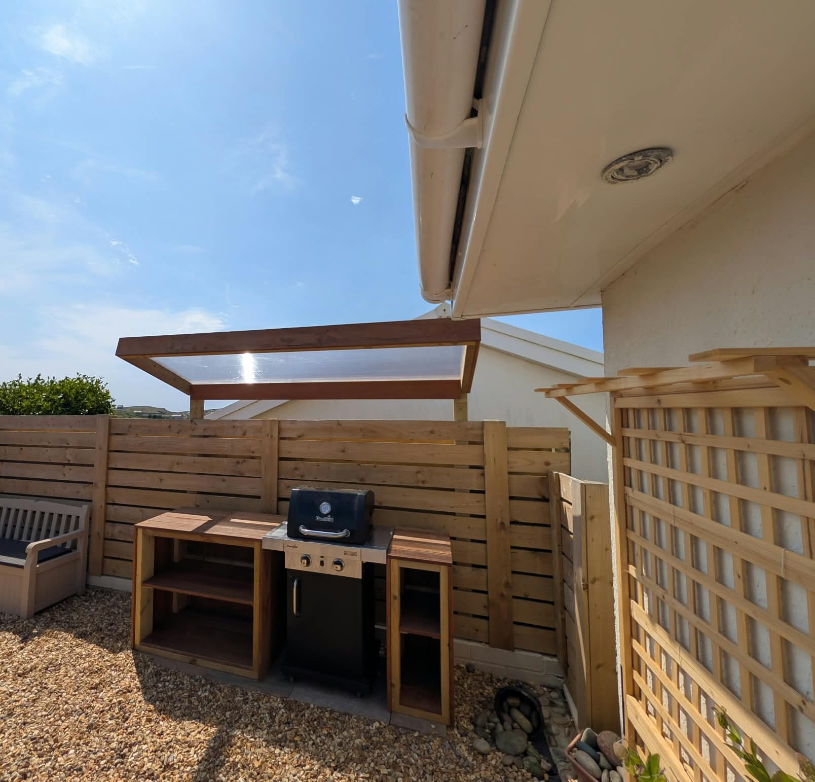 Timber outdoor kitchen canopy and slatted fence on a gravel terrace in Cornwall