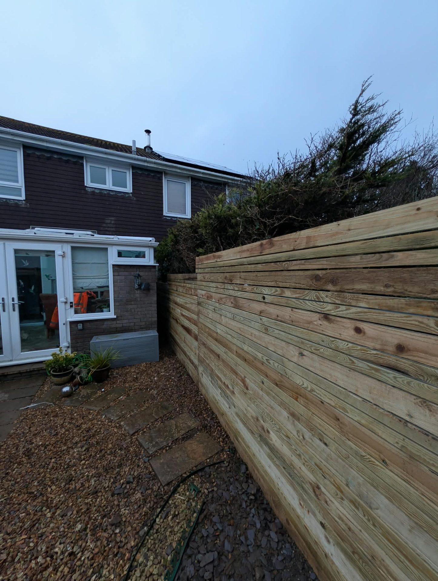Horizontal slatted timber boundary fence beside a gravel path in Cornwall