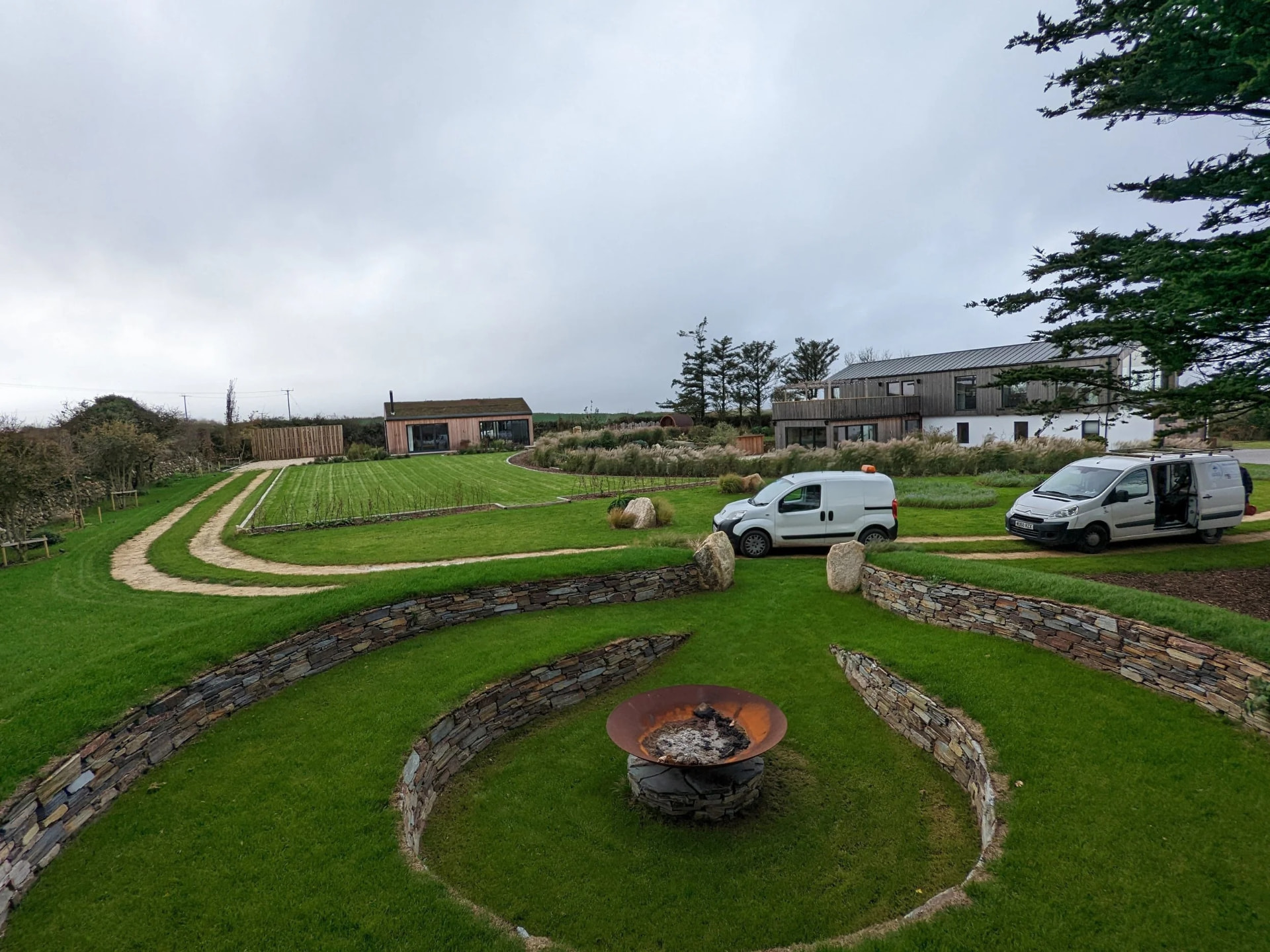 Large Cornish garden with curved stone retaining walls, lawns and a fire pit by Sea Green Landscaping