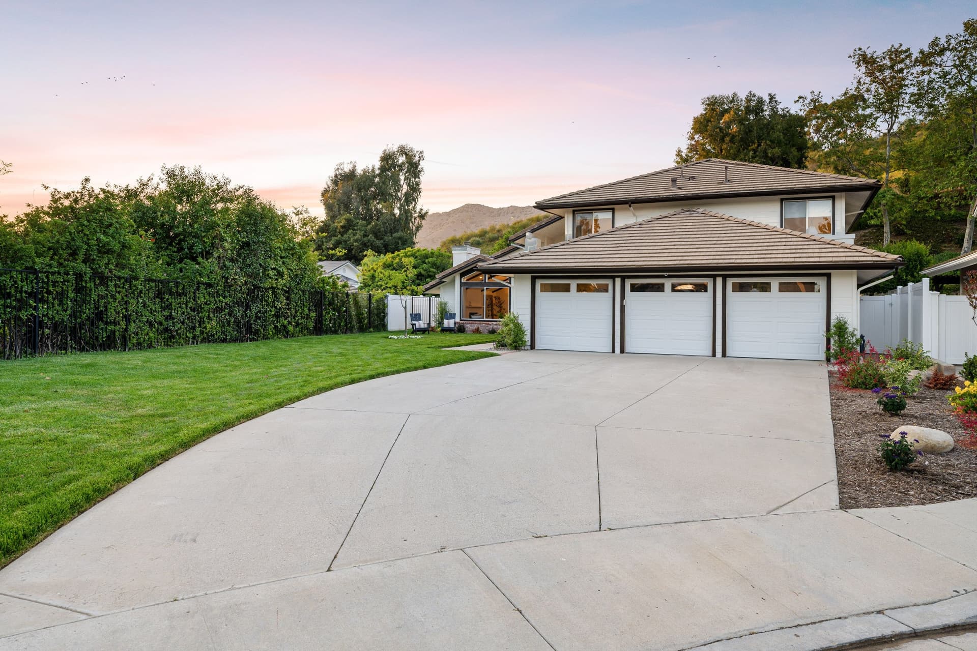 Wide concrete driveway leading to a house with lawn and planted borders