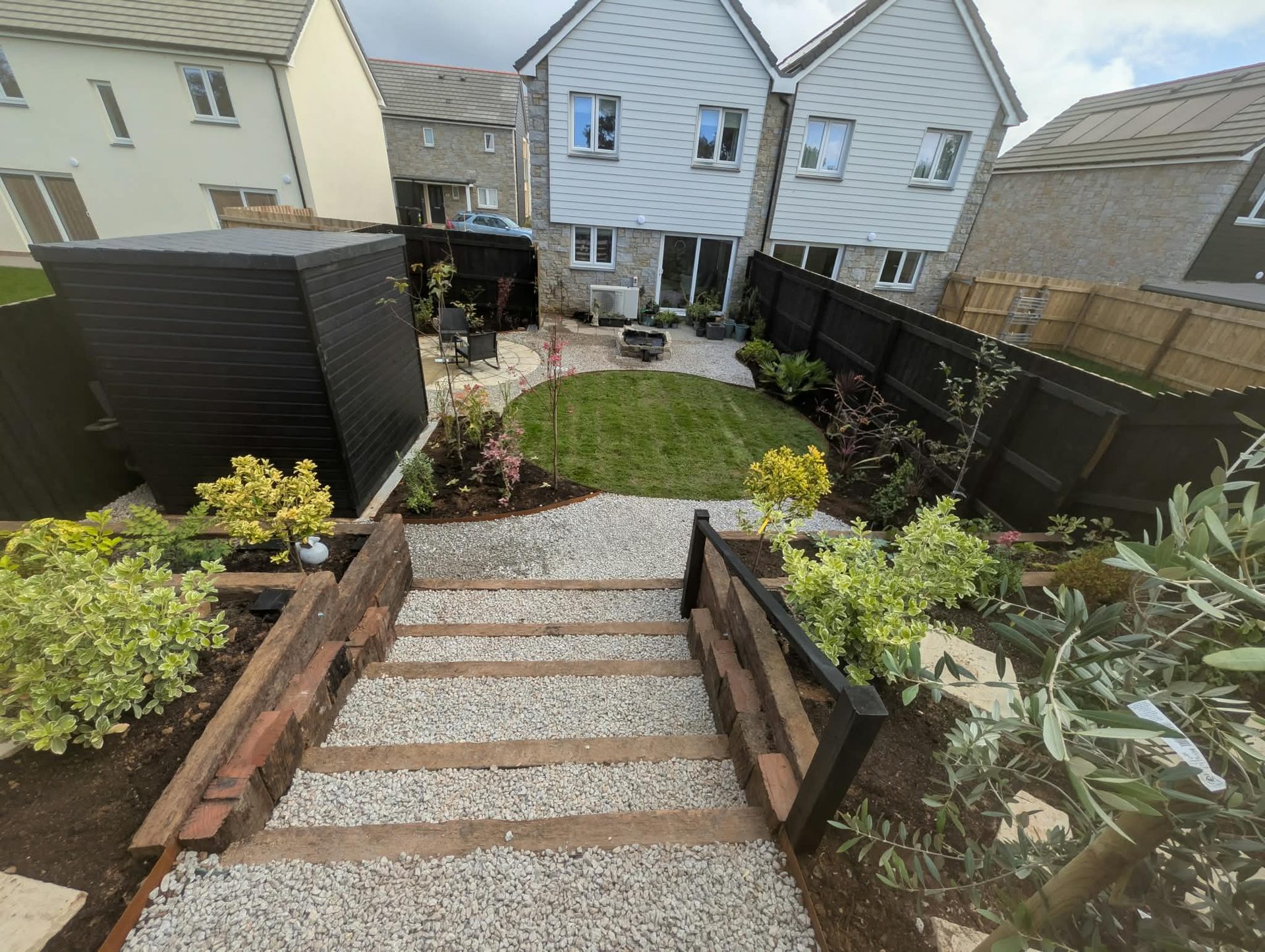 Sleeper and gravel garden steps leading down to a lawn and planted borders in Cornwall
