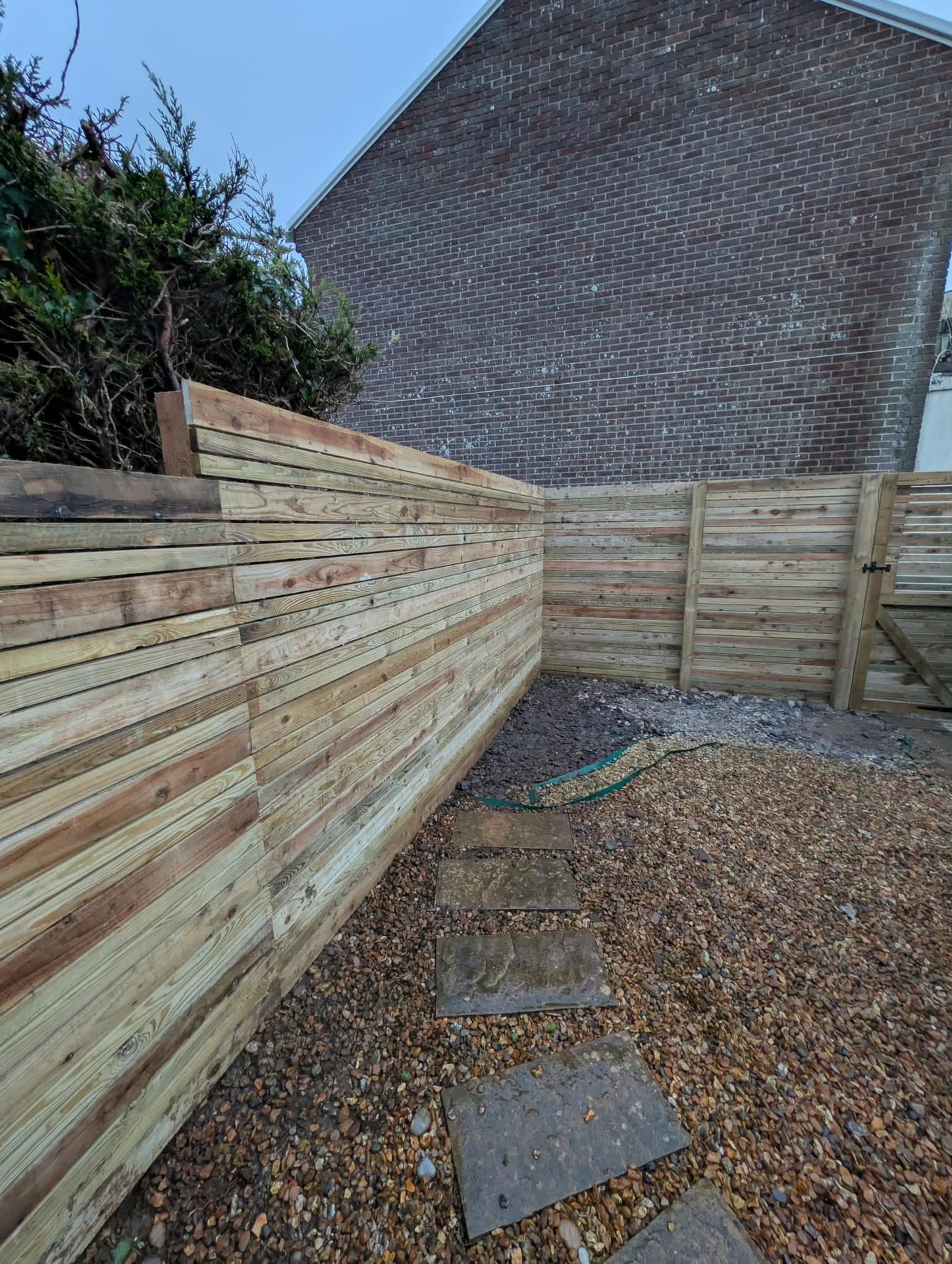 Horizontal slatted timber fence around a gravel garden in Cornwall