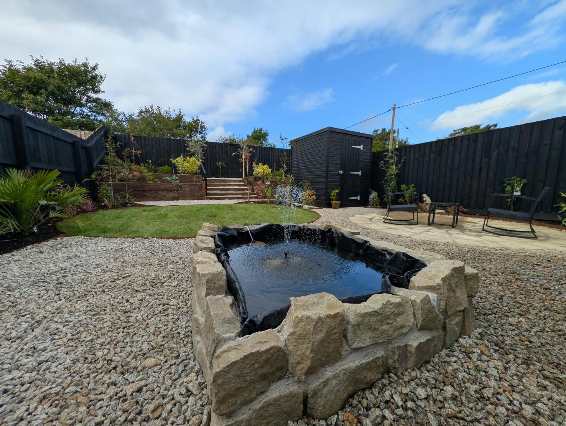 Raised stone pond with fountain set in gravel, part of a garden landscaping project in Cornwall