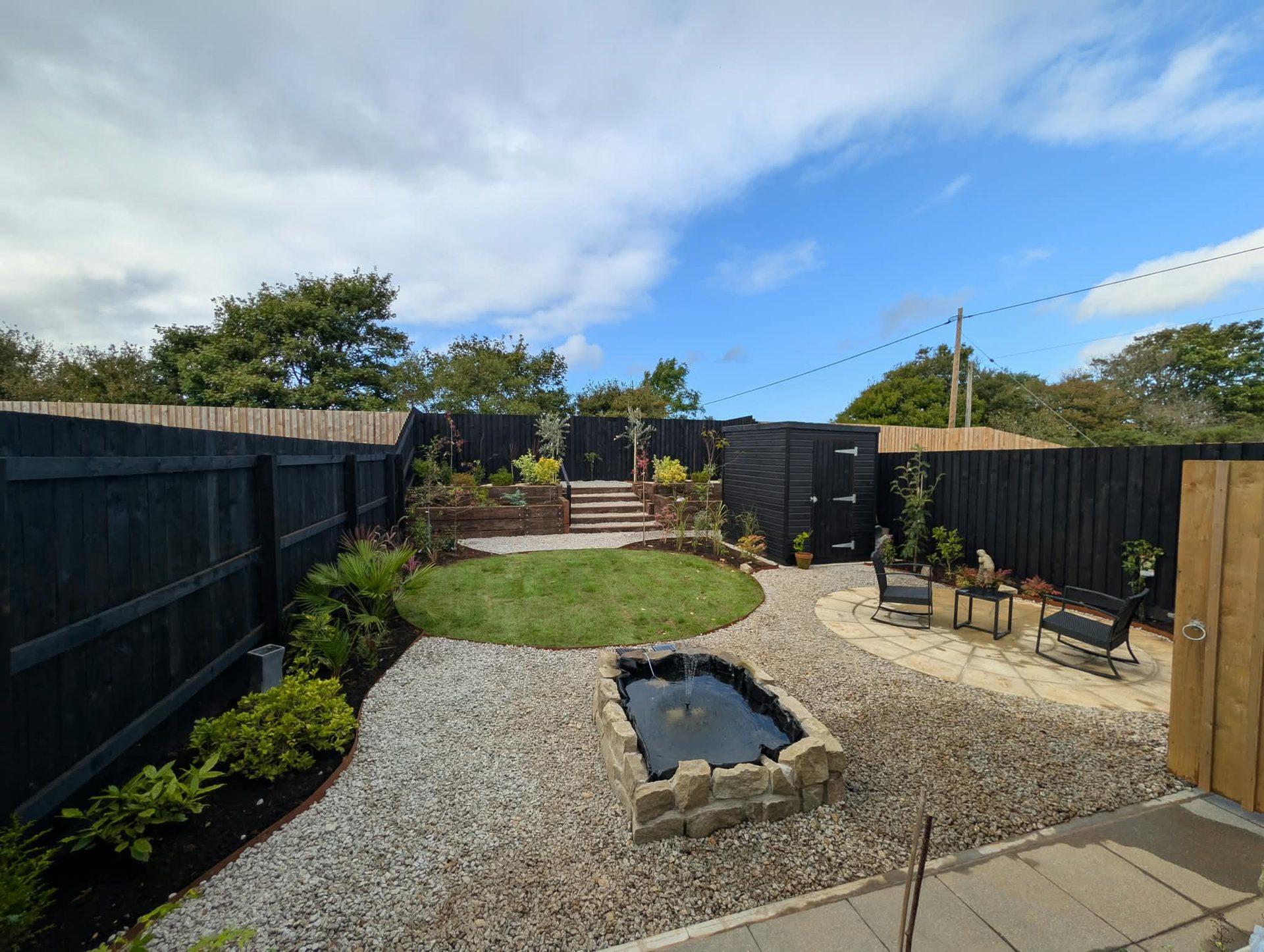 Full garden makeover in Cornwall with lawn, gravel paths, raised pond, sandstone patio and black fencing